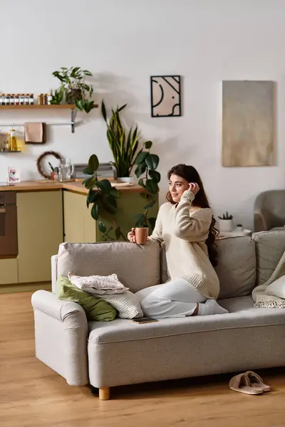 A woman in a cozy sweater sits on a couch, lost in thought while holding a warm cup. — Stock Photo
