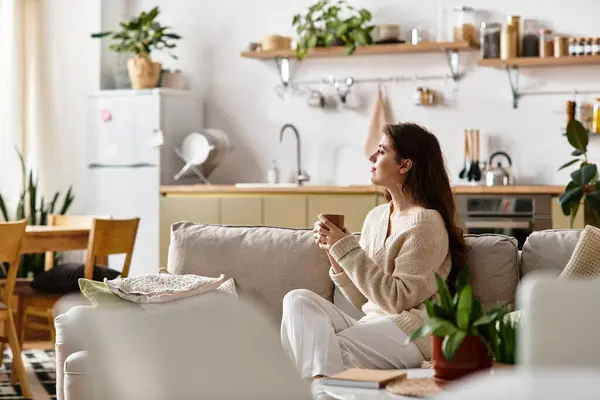 A woman sits quietly on a couch, engaging in deep thought while holding a warm drink. — Stock Photo