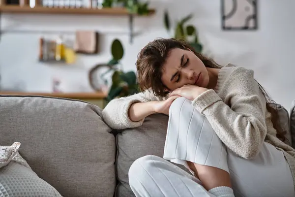 Una donna si siede tranquillamente su un divano, persa nel pensiero mentre affronta le sue emozioni. — Foto stock
