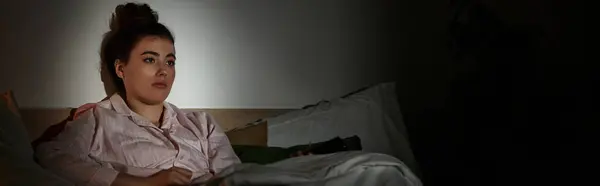 Une jeune femme s'assoit tranquillement au lit, perdue dans ses pensées lors d'une soirée sombre, enveloppée d'ombres. — Stock Photo