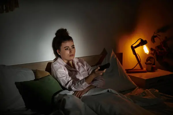 Emotionen entfalten sich, wenn eine Frau allein im Bett sitzt, gedankenverloren, während sie nachts fernsieht. — Stockfoto