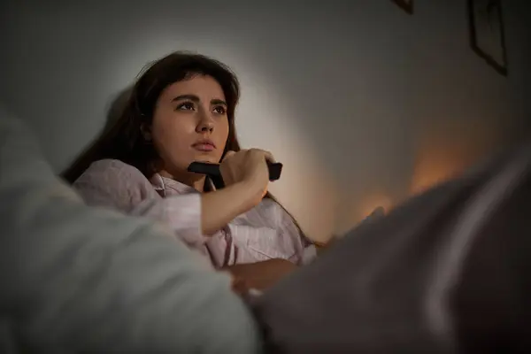 A woman in cozy pajamas sits alone, lost in thought, reflecting on her emotions in dim light. — Stock Photo
