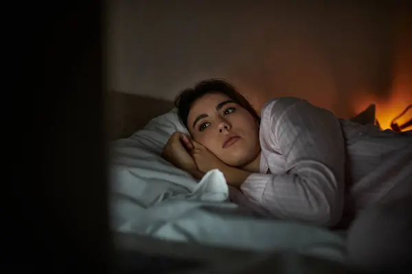 Une femme couchée sur le côté dans son lit, regardant à blanc dans les ténèbres, perdue dans la pensée. — Stock Photo