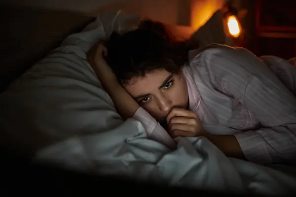 A woman lies on her bed, lost in thought and battling her feelings of sadness and isolation. — Stock Photo