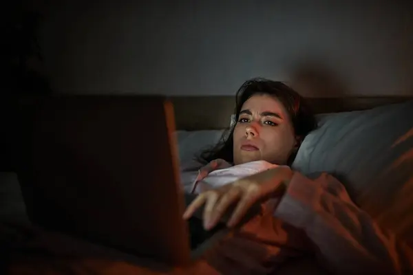 Une femme est couchée, concentrée sur son ordinateur portable, reflétant des sentiments d'isolement et de tristesse. — Stock Photo