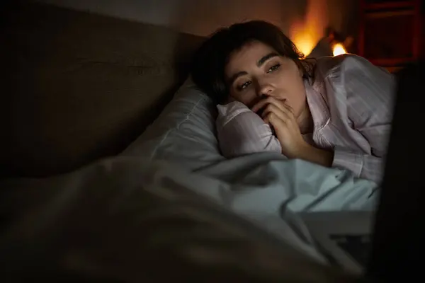 A woman reflects on her feelings while lying in bed late at night, surrounded by dim light. — Stock Photo