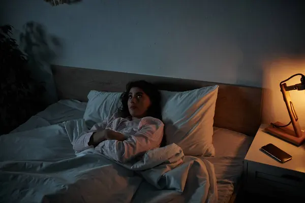 A woman lies in bed, wrapped in blankets, lost in thought as she stares into the dark. — Stock Photo