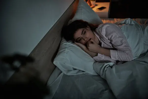 A woman lies on her side, lost in thought under soft bedding, showcasing the weight of her emotions. — Stock Photo