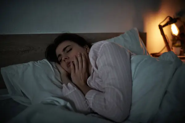 Une femme couchée au lit, les mains couvrant son visage, tandis qu'elle se débat avec ses émotions dans l'obscurité. — Photo de stock