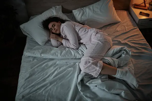 A woman lies curled up in bed, battling her inner turmoil and feelings of sadness as night falls. — Stock Photo