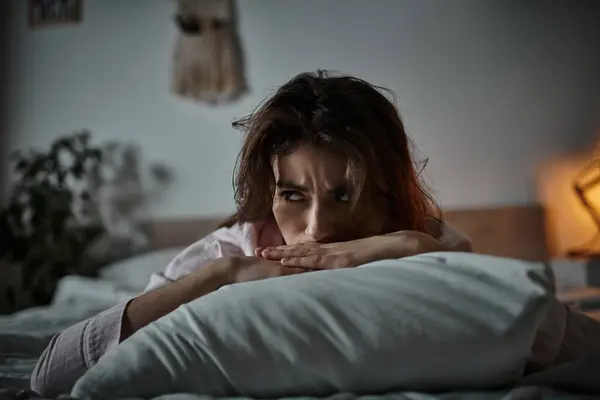 A woman rests her head on a pillow, expressing deep emotions in a dimly lit bedroom space. — Stock Photo