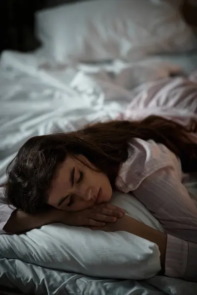 Mulher descansa em um travesseiro em um quarto mal iluminado enquanto luta com suas emoções. — Fotografia de Stock