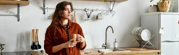 In una cucina confortevole, una donna si perde nel pensiero mentre stringe una tazza calda. — Foto stock