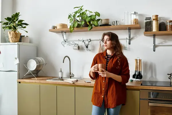 A woman stands quietly in a welcoming kitchen, lost in thought while holding a warm drink. — Stock Photo