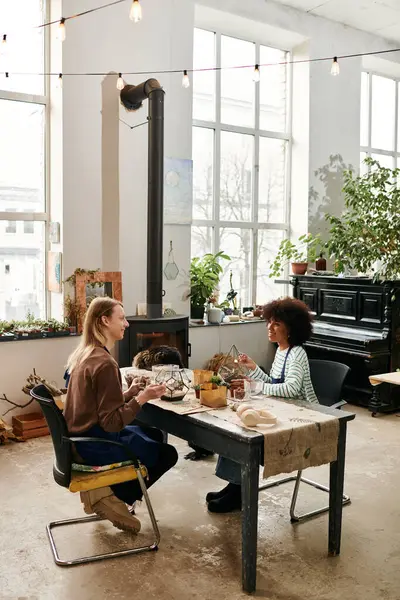 Two friends chat happily at a lively workshop amid lush succulents and greenery. — Stock Photo