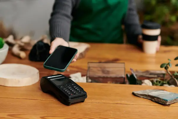 Junge Person mit Telefon an einem Zahlungsterminal in einer grünen Umgebung. — Stockfoto