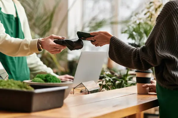 Stylish woman paying with her phone while man working in green setting. — Stock Photo