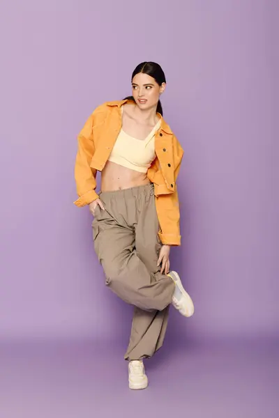 Young woman in a stylish outfit poses playfully against a purple backdrop, exuding confidence. — Stock Photo