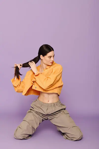 Una mujer joven con estilo muestra su pelo largo y traje de moda contra un telón de fondo púrpura. - foto de stock