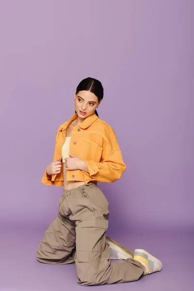 A beautiful young woman poses creatively in a fashionable orange jacket and beige pants. — Stock Photo