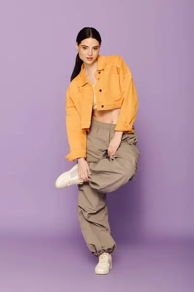 A beautiful woman showcases trendy fashion while playfully posing with one leg raised. — Stock Photo