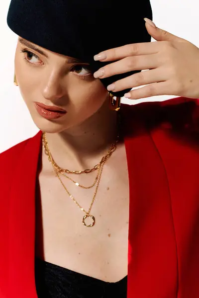 Young woman with a stylish black hat and layered gold chains shows confidence in a vibrant setting. — Stock Photo