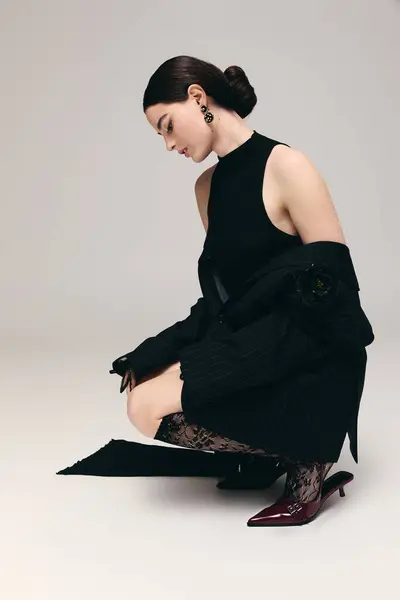 Uma jovem mulher em uma roupa preta ajoelha-se graciosamente, mostrando sua expressão elegante e postura. — Fotografia de Stock
