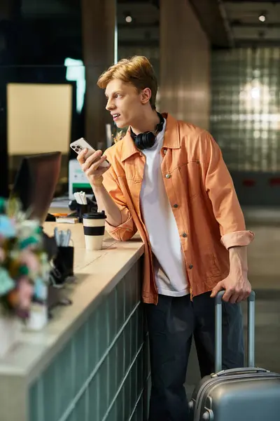 A young man engages with his smartphone while waiting at the hotel reception area. — Stock Photo
