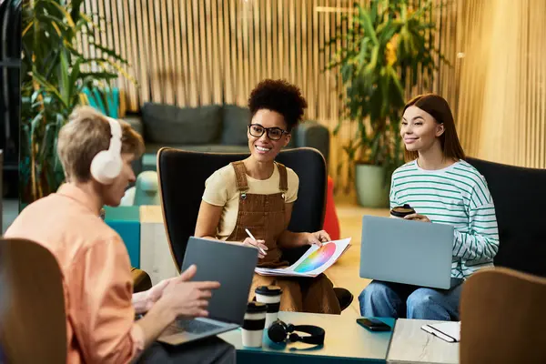 Tre colleghi si impegnano in una vivace discussione mentre lavorano su laptop e condividono idee. — Foto stock