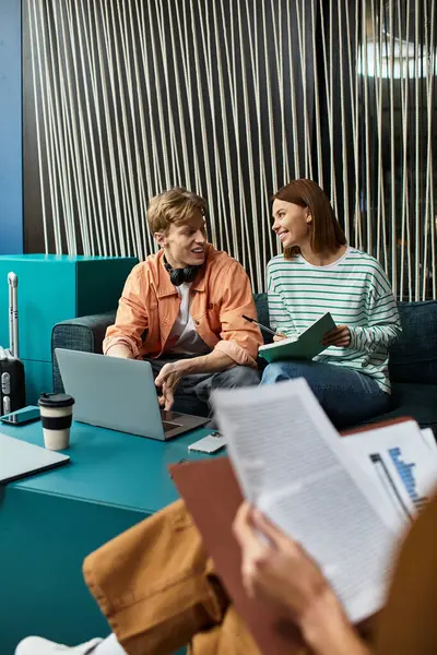 Deux collègues s'engagent dans une discussion animée tout en travaillant sur leurs ordinateurs portables dans un salon d'hôtel. — Photo de stock
