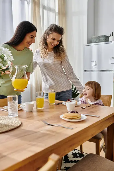 Two women joyfully make a vibrant breakfast for their daughter in a warm, stylish apartment. — Stock Photo