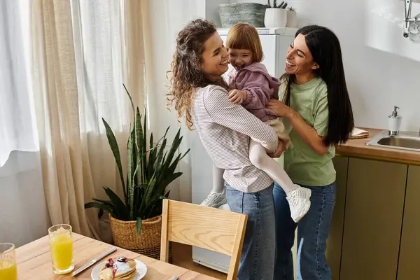 Two loving mothers embrace their daughter while sharing playful moments in their cozy home. — Stock Photo