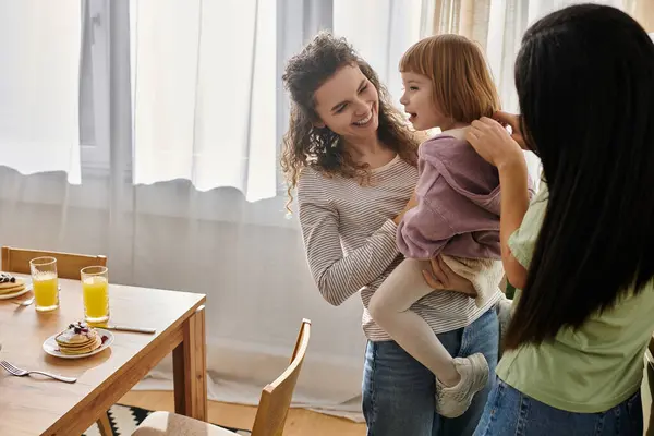 Two women celebrate family life while playfully engaging with their daughter in a cozy space. — Stock Photo