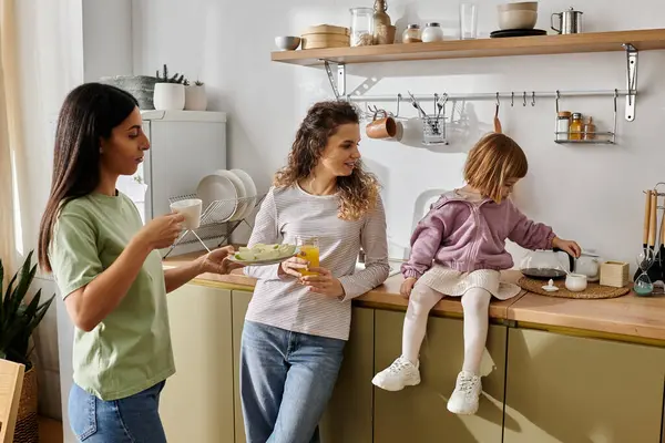 Two women share a delightful morning while their daughter plays and explores in their cozy kitchen. — Stock Photo