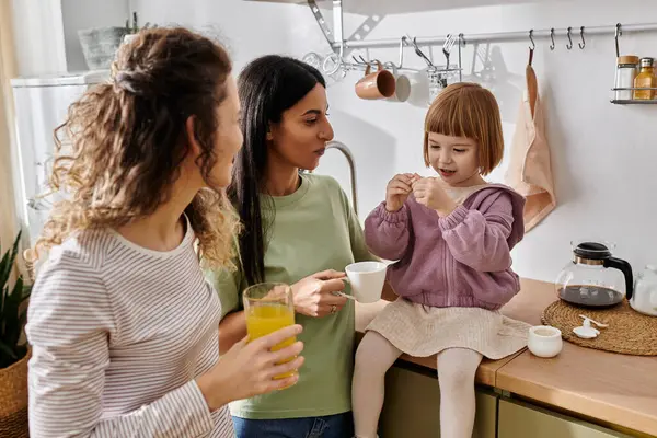 Dos mujeres comparten un momento cálido en su cocina moderna mientras disfrutan de la compañía de su hija. - foto de stock