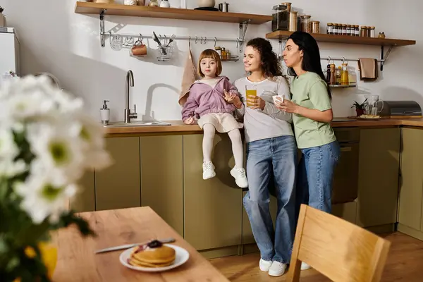 Two women enjoy breakfast while playfully engaging their daughter in their stylish kitchen. — Stock Photo