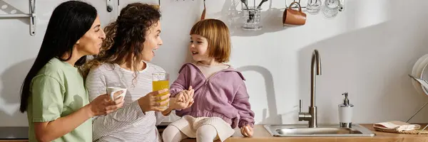 Zwei Frauen unterhalten sich fröhlich mit ihrer Tochter in einer modernen Küche bei Drinks, Banner — Stockfoto