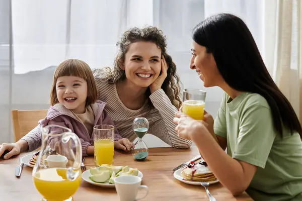 Two women share a cheerful breakfast with their smiling daughter in a bright space. — Stock Photo