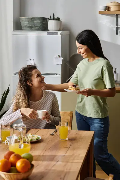 Two happy lesbian women enjoy a light meal together in their stylish apartment while smiling and connecting. — Stock Photo