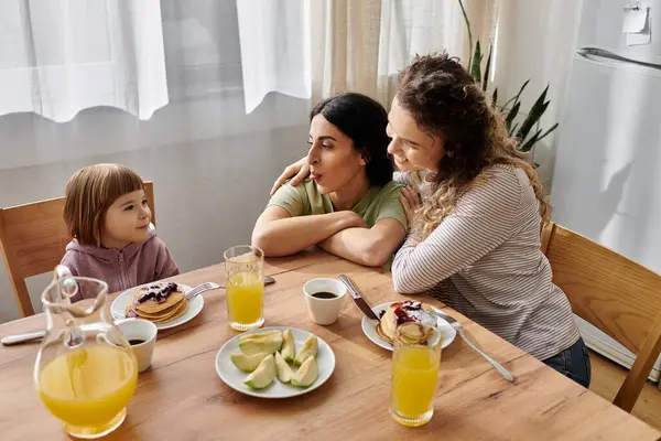 Two women share a joyful breakfast with their daughter in a bright, modern apartment. — Stock Photo