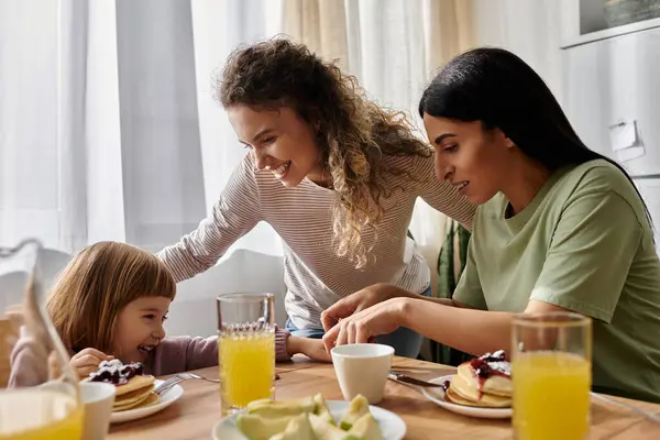 Deux femmes interagissent amoureusement avec leur fille lors d'un petit déjeuner gai à la maison. — Photo de stock