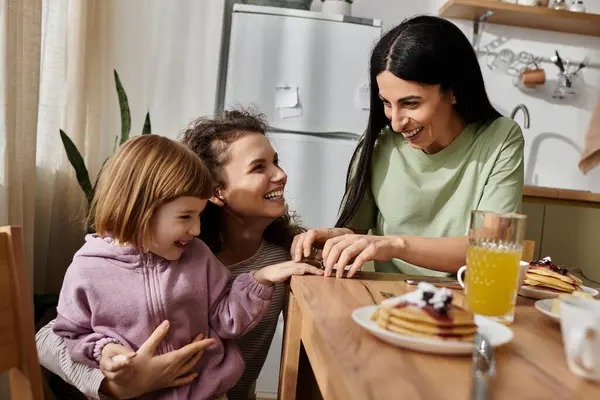 Due donne gioiose condividono frittelle e risate con la figlia in uno spazio accogliente e moderno. — Foto stock