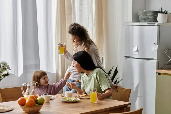 Two mothers share a delightful morning with their daughter, enjoying breakfast and laughter. — Stock Photo