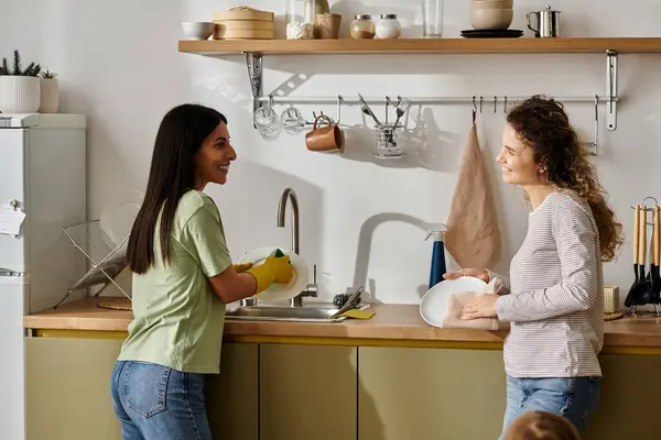Glückliches lesbisches Paar teilt einen unbeschwerten Moment beim Geschirrspülen in ihrer stilvollen Wohnung. — Stockfoto