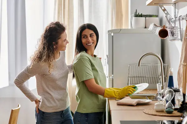 Zwei fröhliche Frauen teilen Lachen und Liebe, während sie ihre gemütliche Wohnküche aufräumen. — Stockfoto