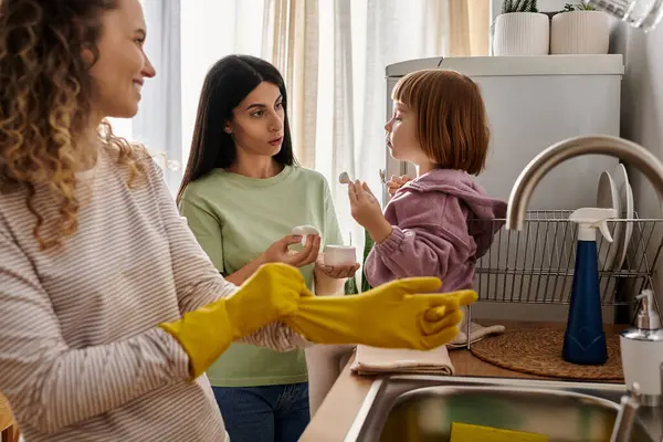 Dos madres se relacionan con su hija en una cocina luminosa y moderna. - foto de stock