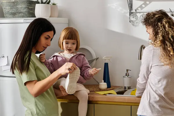 Zwei Frauen interagieren, während ihre Tochter ihre Umgebung in einer gemütlichen Küche erkundet. — Stockfoto