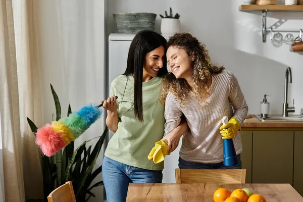 Joyful lesbian couple smile at each other, engaging in playful cleaning in their stylish home. — Stock Photo