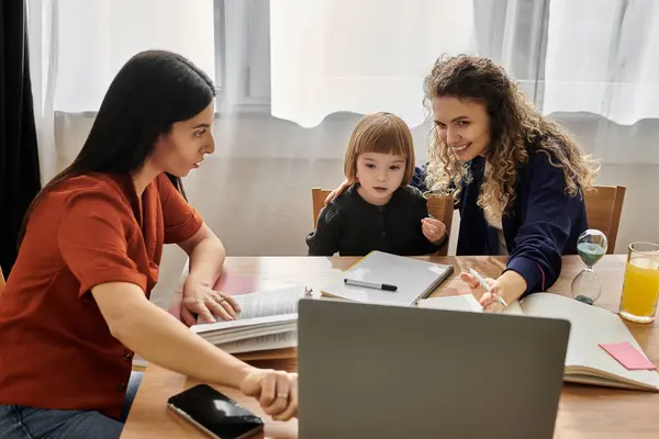 Two women engage with their daughter at a table, sharing smiles and learning in their cozy space. — Stock Photo