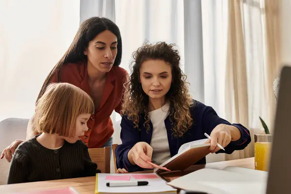 Dos mujeres y su hija disfrutan de un tiempo de calidad juntos mientras exploran un libro en un acogedor apartamento. - foto de stock